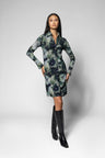 A woman modeling a long-sleeve collared dress with a dark green and navy floral pattern, paired with black knee-high boots, against a light gray studio background.