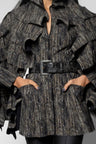 A close-up of a model wearing a black and gray vertically striped ruffled jacket with a matching belt and a large square buckle.
