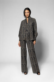A model stands against a light gray studio background wearing a matching dark gray and black patterned two-piece suit with a long-sleeve jacket and wide-leg trousers.