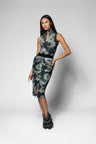 A model wearing a sleeveless high-neck shirt and midi skirt with a green and black abstract floral pattern, paired with black ankle boots, against a light gray studio background.