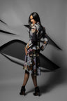 A model wearing a long-sleeved, knee-length floral print coat with black high heels, posed against a dark gray background with abstract layered paper-like shapes.