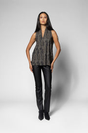 A model stands against a light gray studio background wearing a sleeveless textured top with a dark gray and black mottled pattern, paired with black pants and black ankle boots.