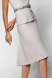 A woman wearing a light gray knee-length skirt with a structured peplum waist and a patterned belt, shown against a plain light gray studio background.