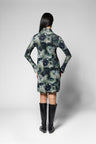 A model viewed from the back wearing a long-sleeve collared dress with a dark floral watercolor pattern in navy, green, and gray, paired with black knee-high boots, against a light gray studio background.