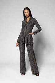A model wearing a dark gray and black textured two-piece suit with a two way zip up jacket and matching wide-leg trousers, standing against a light gray studio background.