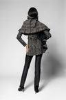 A model shown from the back wearing a textured, dark gray and black ruffled scarf over matching jacket with long sleeves, paired with black pants and black high heels, against a light gray studio background.
