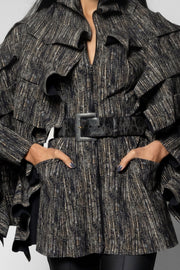 A close-up of a model wearing a black and gray vertically striped ruffled jacket with a matching belt and a large square buckle.