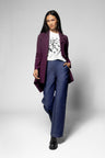 A woman modeling a dark purple blazer, blue wide-leg trousers, a white graphic t-shirt, and black boots against a light gray studio background.