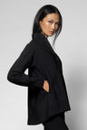 A woman modeling a black long-sleeve jacket with a high stand collar, shown from a three-quarters back angle against a light gray studio background.