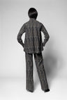 A model shown from the back wearing a matching dark gray and black textured patterned blazer and trousers set, photographed against a neutral light gray studio background.