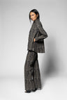 A model wearing a matching textured gray and black jacket and wide-leg trousers suit, standing in profile against a light gray studio background.