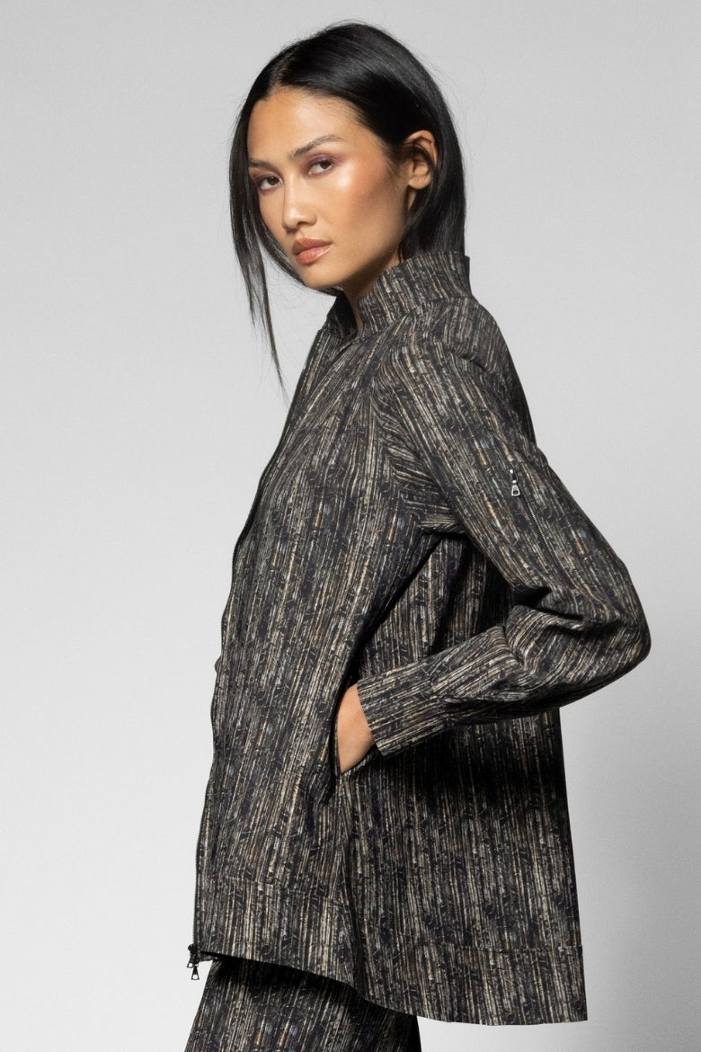 A model wearing a dark gray and black textured, vertically-striped blazer with a high collar, photographed against a neutral light gray studio background.