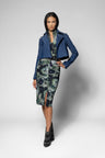 A model stands against a light gray studio background wearing a blue cropped jacket over a green and blue patterned top and matching green and blue patterned skirt, with black studded ankle boots.