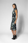 A woman modeling a sleeveless high-neck top and midi skirt with a dark green, black, and gray abstract floral print, paired with black studded ankle boots, against a light gray studio background.