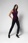 A woman modeling a sleeveless, ruched deep purple top paired with black pants and black ankle boots, standing against a light gray studio background.