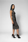 A woman modeling a sleeveless, high-neck top and matching skirt with a textured black and gray pattern, paired with black high-heeled shoes, against a light gray studio background.