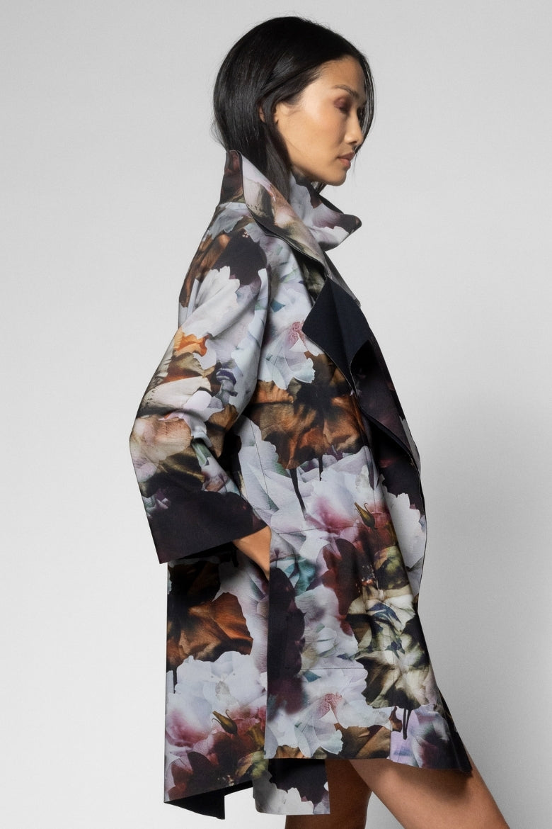 A woman shown in side profile wearing a long floral print coat with a high collar, photographed against a plain light gray studio background.