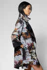 A woman shown in side profile wearing a long floral print coat with a high collar, photographed against a plain light gray studio background.