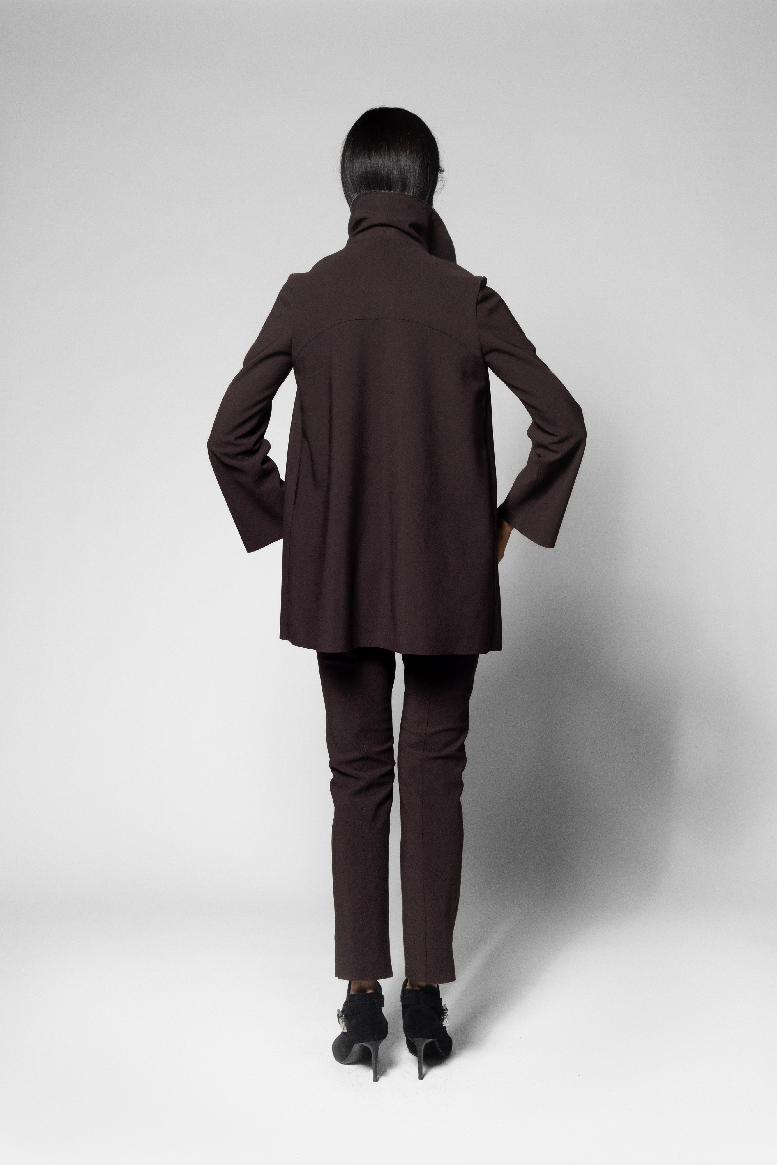 A model viewed from the back wearing a dark brown tailored blazer and matching slim trousers with black heels, set against a light gray studio background.