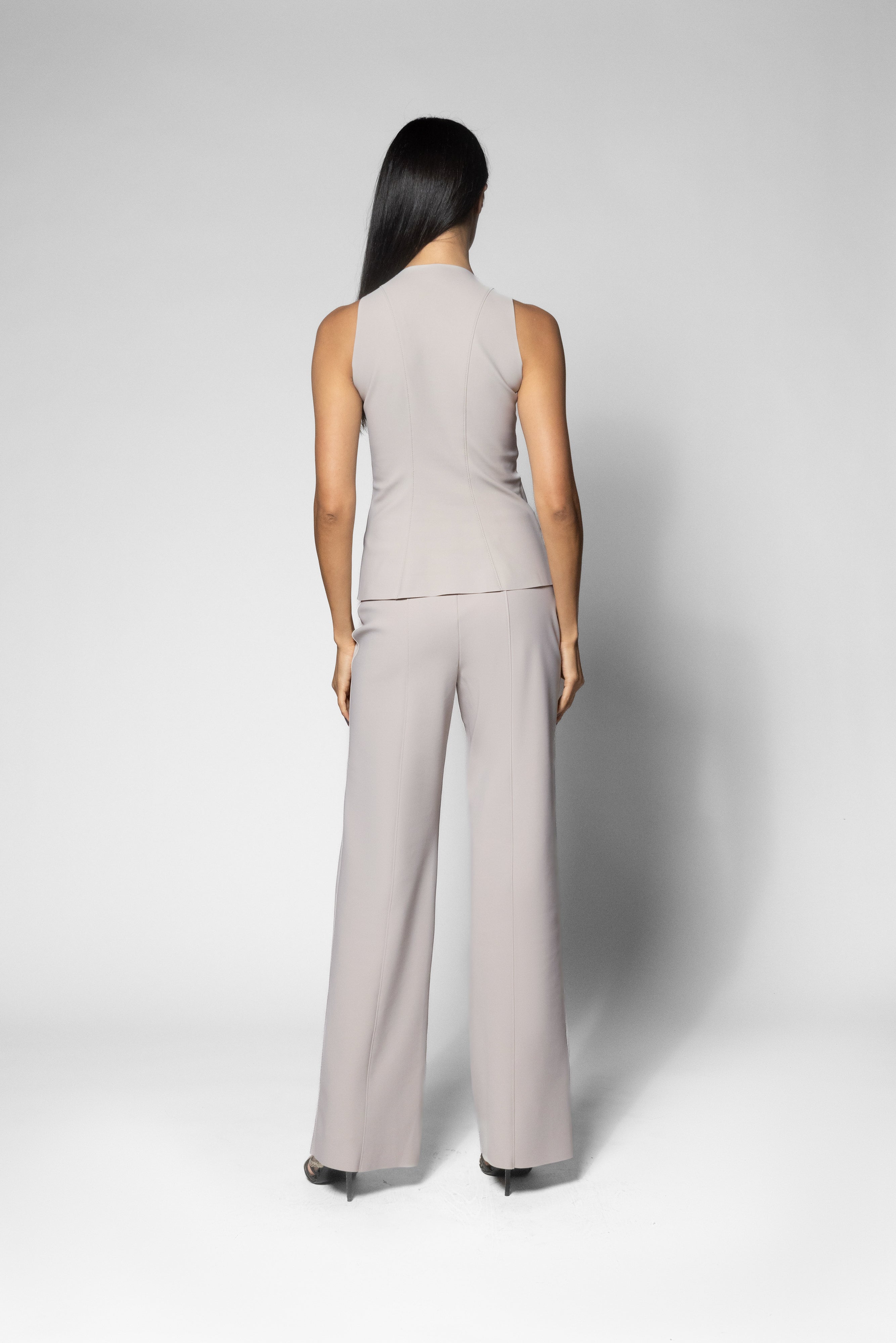 A model shown from the back wearing a light beige sleeveless top and matching wide-leg trousers, photographed against a neutral light gray studio background.