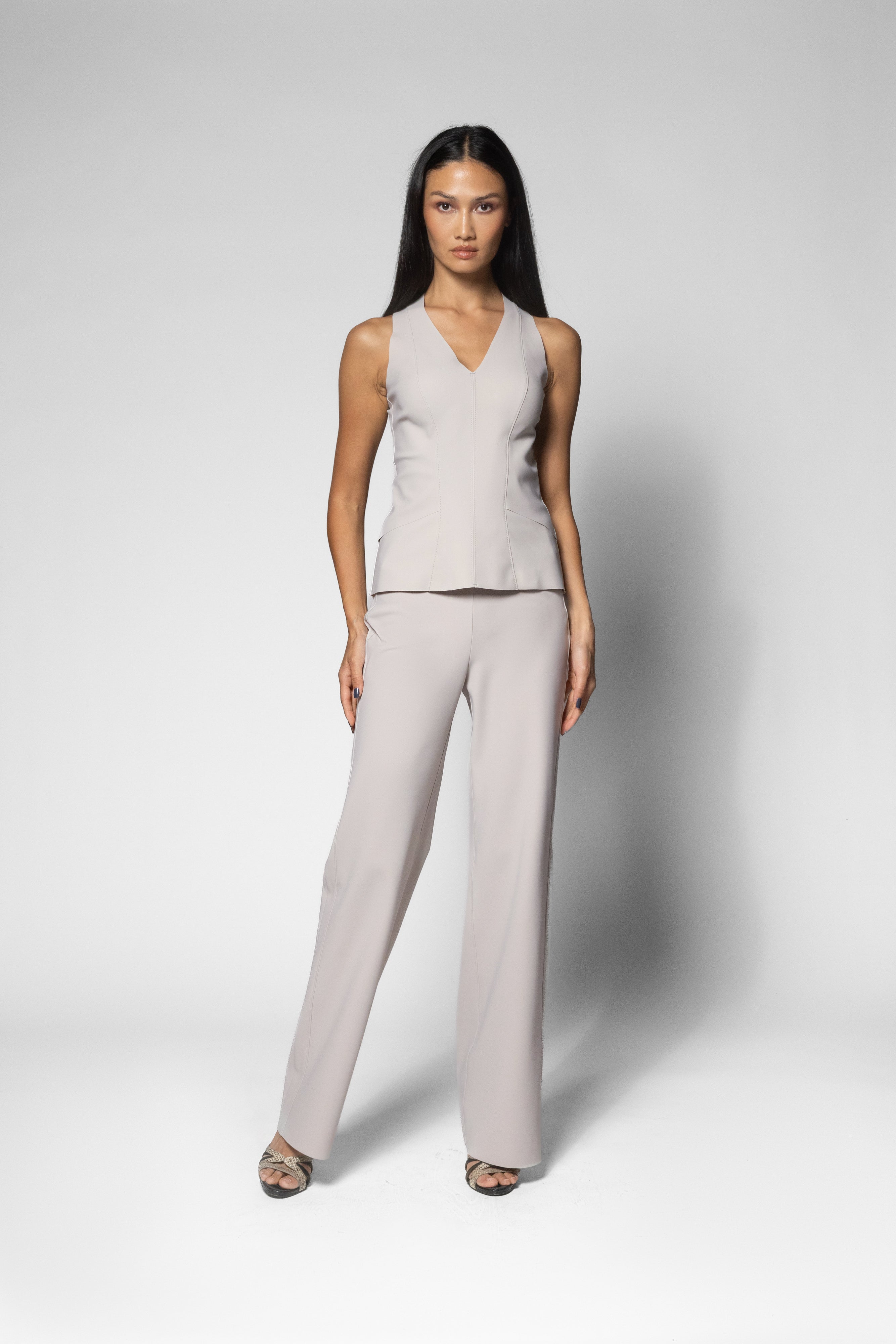 A woman modeling a light beige sleeveless wrap-style top and matching wide-leg trousers set against a neutral gray studio background.