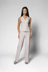 A woman modeling a light beige sleeveless wrap-style top and matching wide-leg trousers set against a neutral gray studio background.