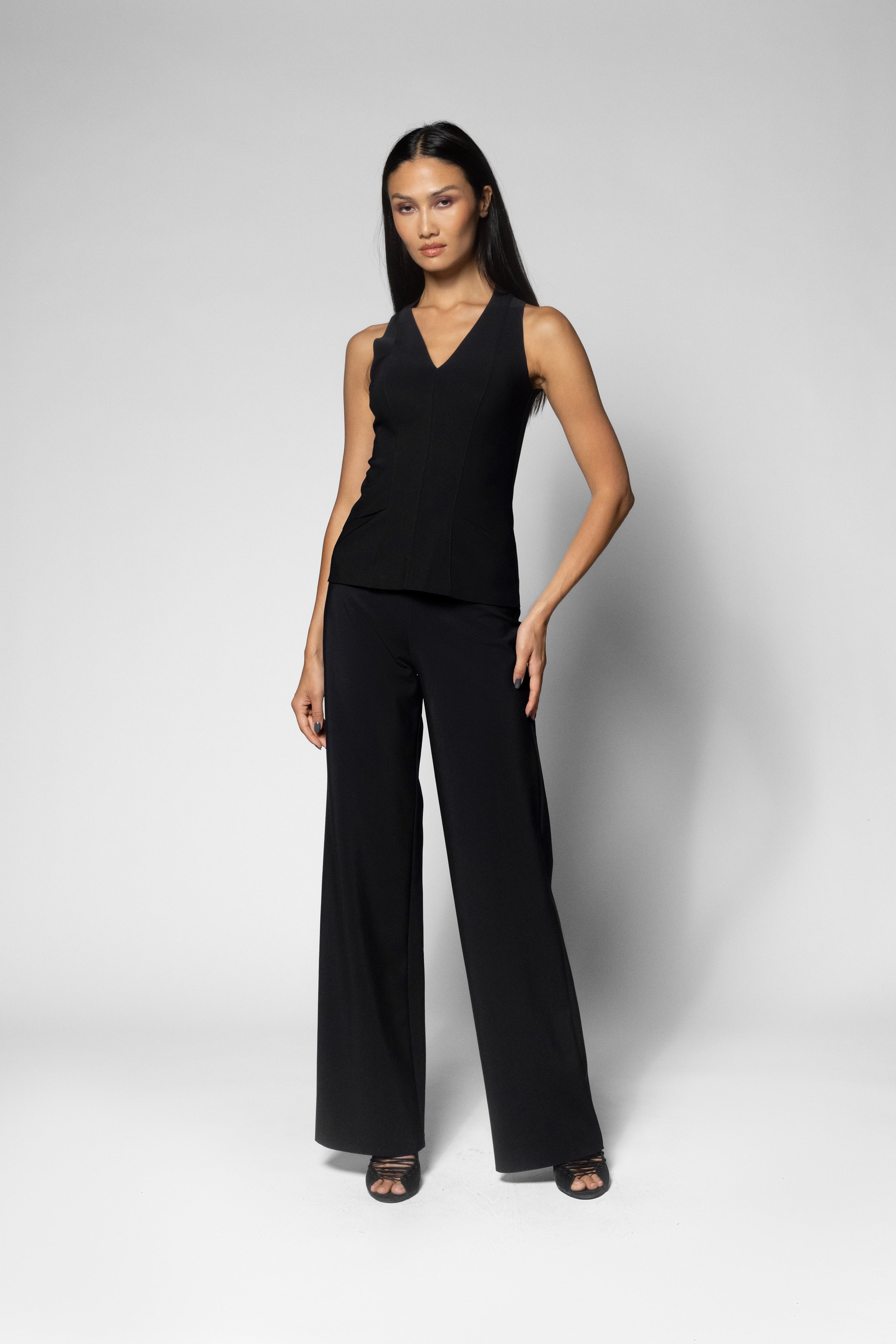 A woman modeling a black sleeveless vest top and matching wide-leg trousers against a light gray studio background.