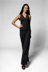 A woman modeling a black sleeveless V-neck top and matching black wide-leg pants against a light gray studio background.