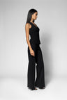 A woman modeling a black sleeveless top and matching wide-leg pants, shown in profile against a light gray studio background.