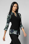 A woman modeling a black vest and long-sleeve blouse with green and blue floral watercolor patterned sleeves, collar, and hem, paired with black pants against a light gray studio background.