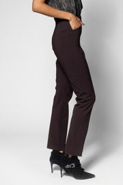 A model wearing dark plum-colored straight-leg trousers, paired with black pointed-toe stiletto heels, shown from the waist down against a light gray studio background.