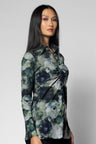 A woman modeling a long-sleeve button-up blouse with a dark green, gray, and black floral watercolor pattern, photographed against a neutral light gray background.
