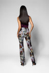 A woman shown from the back wearing high-waisted, wide-leg trousers with a multicolor floral and butterfly print, paired with a dark sleeveless top and black heels, against a light gray studio background.