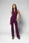 A woman modeling a sleeveless, deep plum-colored V-neck top and matching flattering seamed wide leg pants, standing against a light gray studio background.