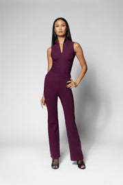 A woman modeling a sleeveless, deep plum-colored V-neck top and matching flattering seamed wide leg pants, standing against a light gray studio background.