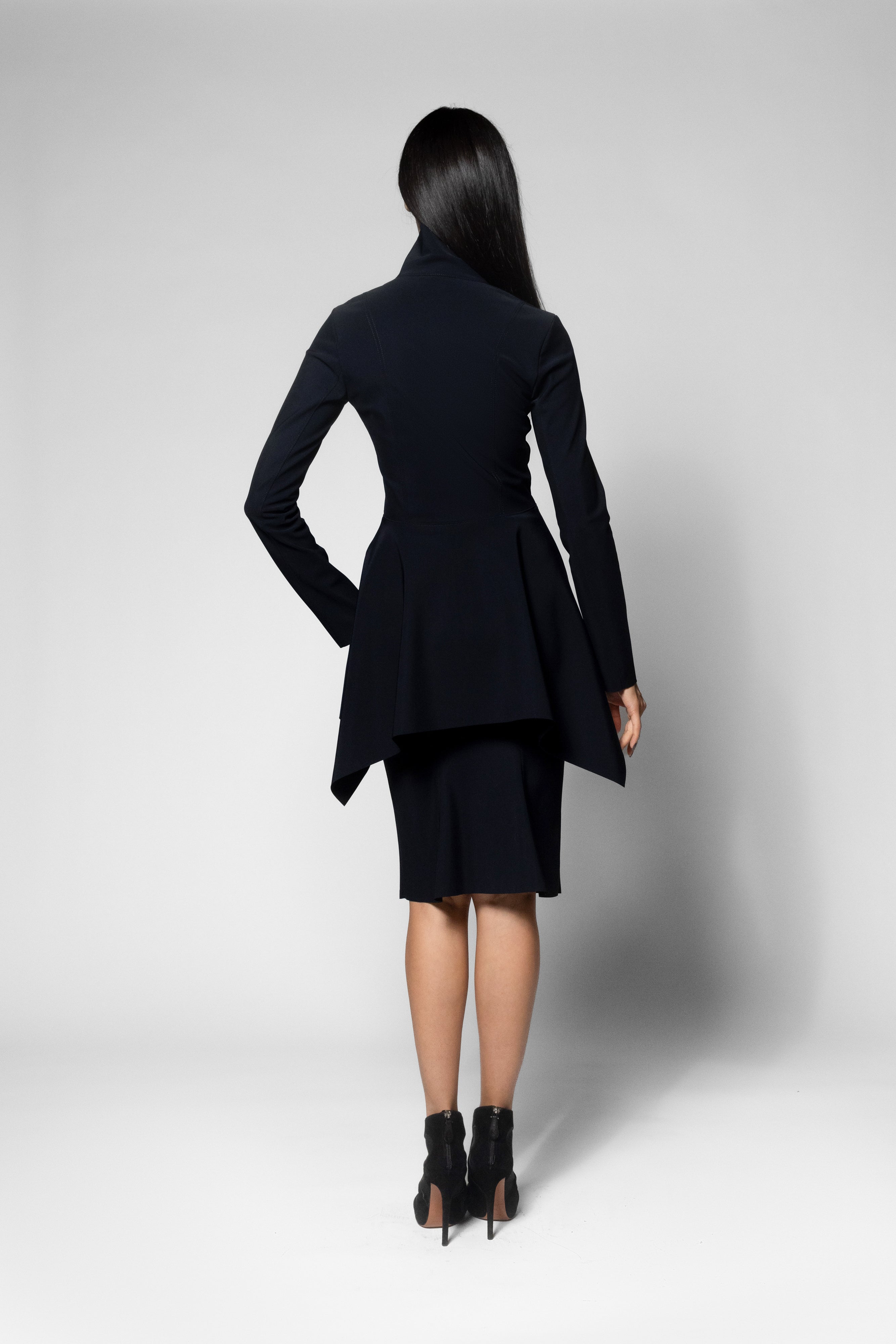A woman shown from the back wearing a black long-sleeve peplum-style jacket with a high collar and black ankle boots, photographed against a light gray studio background.