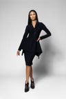 A woman modeling a black tailored two-piece outfit consisting of a long-sleeve peplum-style blazer with a front zipper and matching knee-length skirt, posed against a light gray studio background.