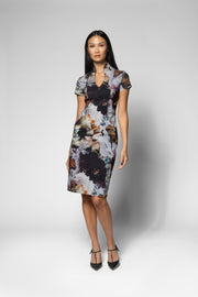 A woman modeling a short-sleeve knee-length dress with a dark floral print over a light gray base, paired with black pointed-toe heels, against a light gray studio background.