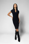 A woman modeling a short-sleeve black bodycon dress with a V-neckline, paired with black knee-high boots, against a light gray studio background.