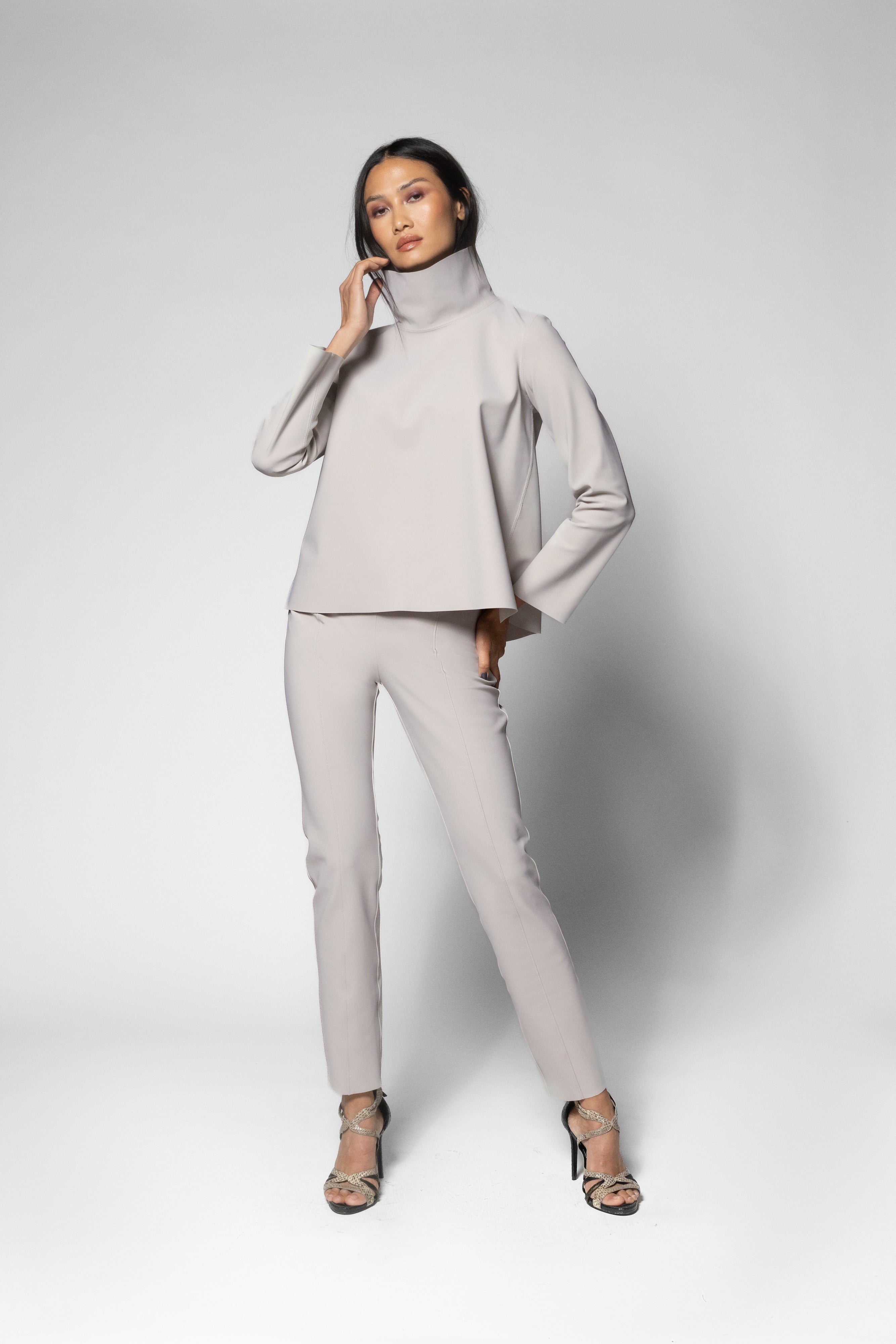 A model wearing a light gray two-piece set consisting of a long-sleeve mock-neck top and matching slim-fit pants, paired with leopard-print high heels, against a light gray studio background.