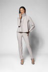 A woman modeling a light gray two-piece outfit consisting of a long-sleeve mock-neck top and matching slim-fit pants, paired with high heels, against a light gray studio background.
