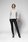 A model stands against a light grey studio background wearing a light beige long-sleeve mock-neck top, black pants, and black lace-up high-heeled sandals.