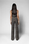 A woman viewed from the back wearing a sleeveless, high-waisted jumpsuit with wide legs in a textured black and gray pattern, set against a plain light gray studio background.