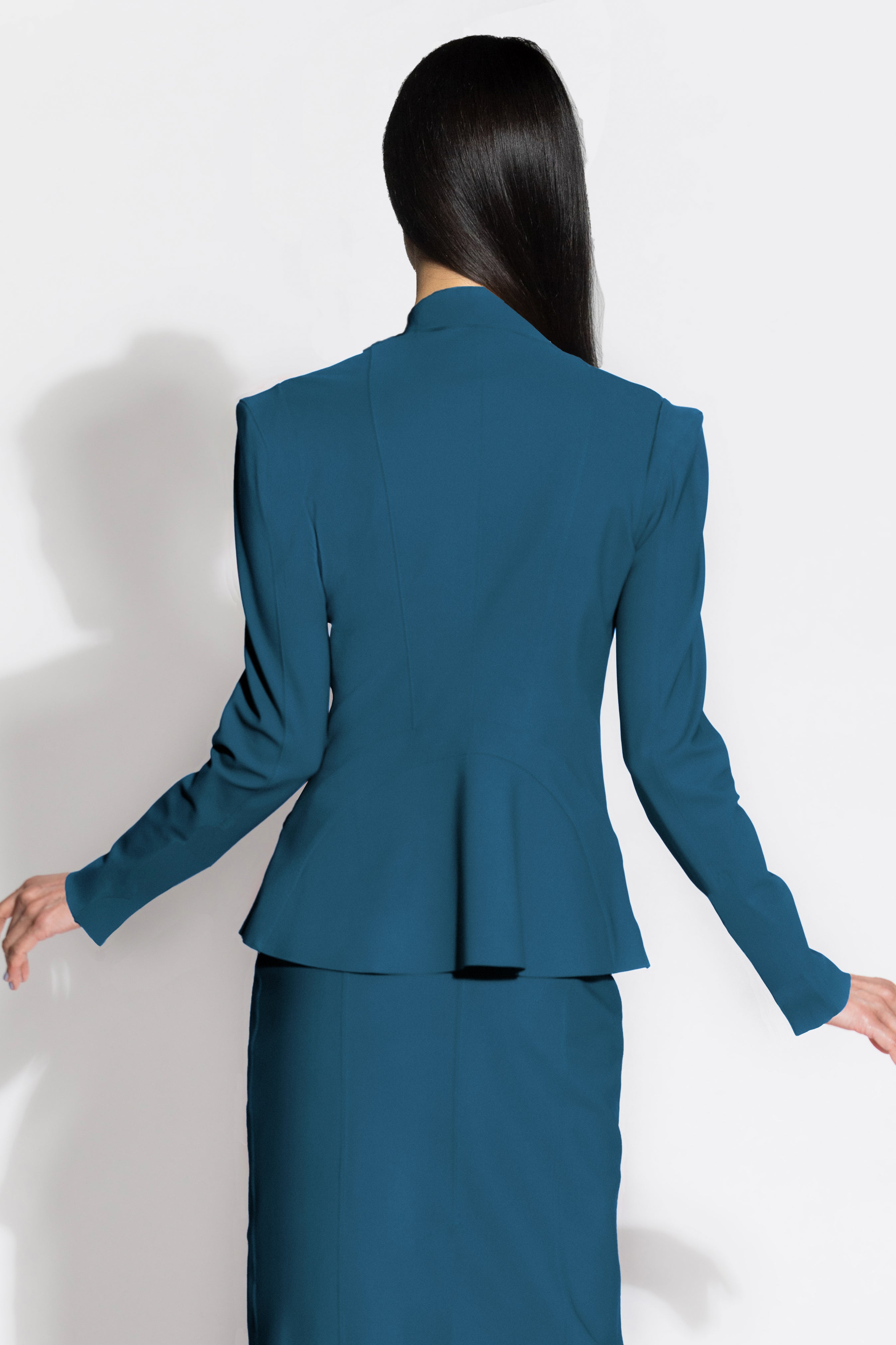 A woman shown from the back wearing a teal blue tailored blazer with structured shoulders and a matching fitted skirt against a plain light background.