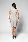 A woman viewed from the back wearing a sleeveless light beige knee-length dress with a central zipper, paired with black high heels, against a light gray studio background.