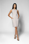 A woman modeling a sleeveless, knee-length bodycon dress in a light beige, paired with strappy high-heeled sandals, against a light gray studio background.