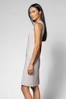 A woman modeling a sleeveless, knee-length light beige dress against a plain light gray studio background.