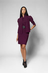 A model wearing a deep plum purple two-piece suit consisting of a structured jacket with puffed sleeves and a matching pencil skirt, paired with black ankle boots, against a light gray studio background.