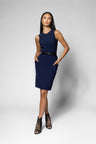 A woman modeling a sleeveless navy blue knee-length dress with a black belt at the waist, paired with black lace-up heeled sandals, against a light gray studio background.