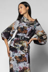 A model wearing a floral print skirt and top with a black belt, photographed against a neutral gray studio background.